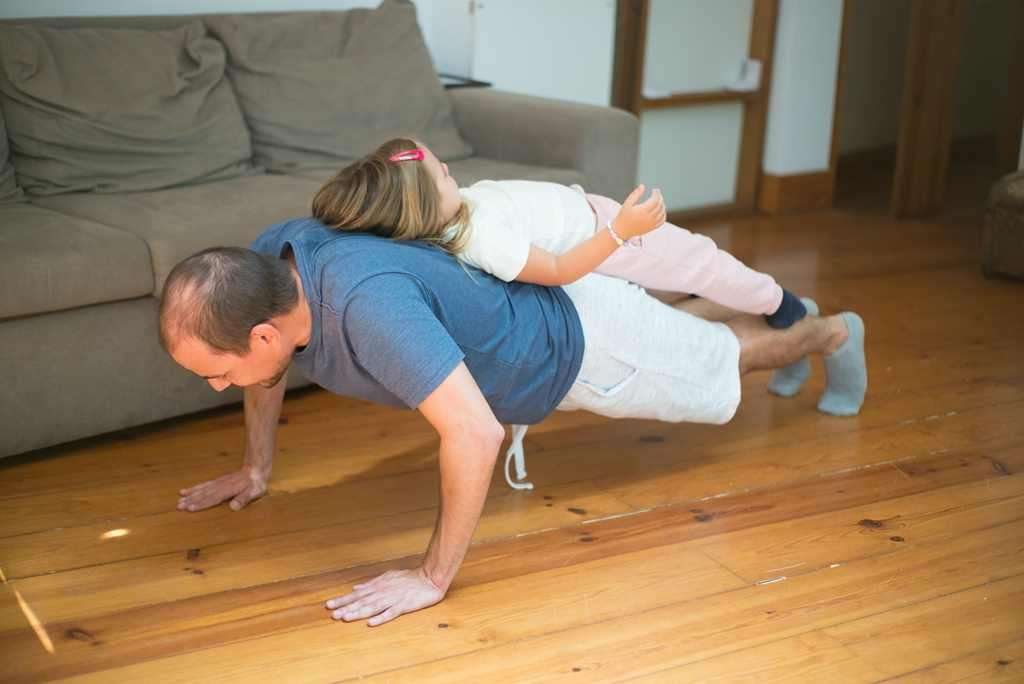 Man doing push ups with daughter lying on his back